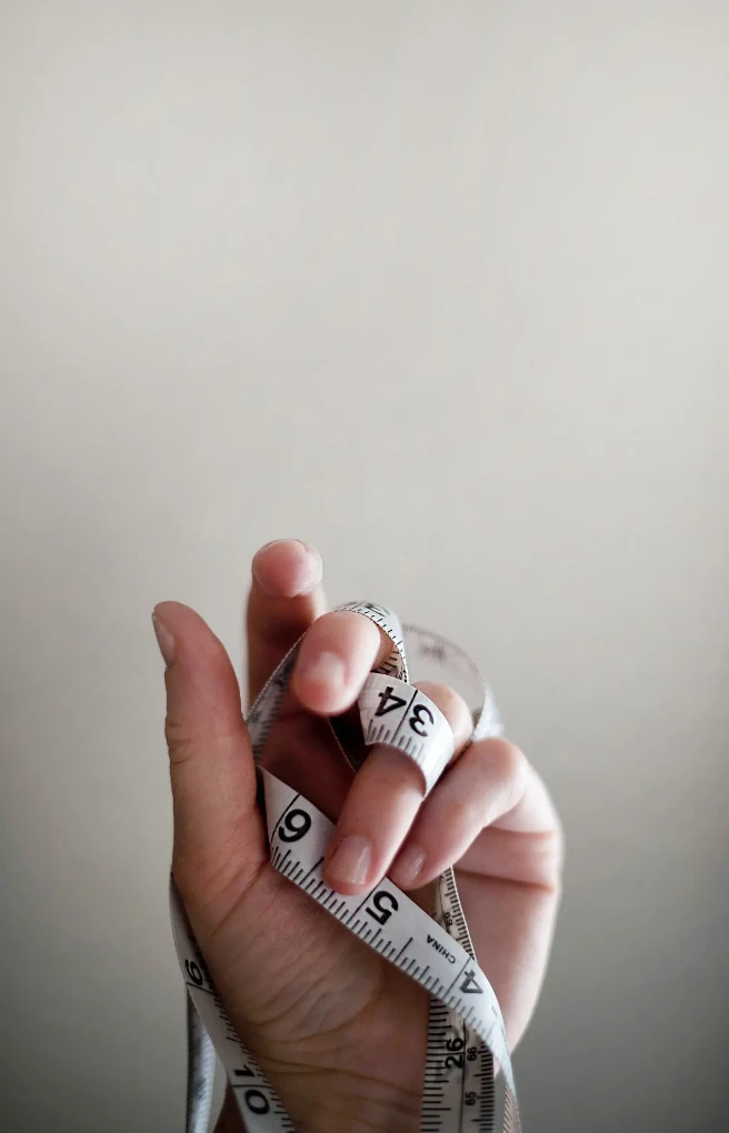 A hand is holding a flexible tape measure, a tool used for measuring length or body dimensions